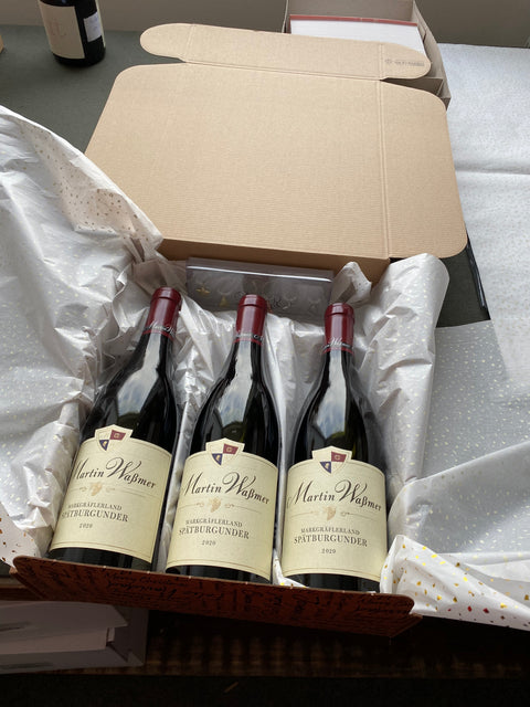 Ein Geschenpaket mit drei Flaschen Rotwein und Seidenpapier. 